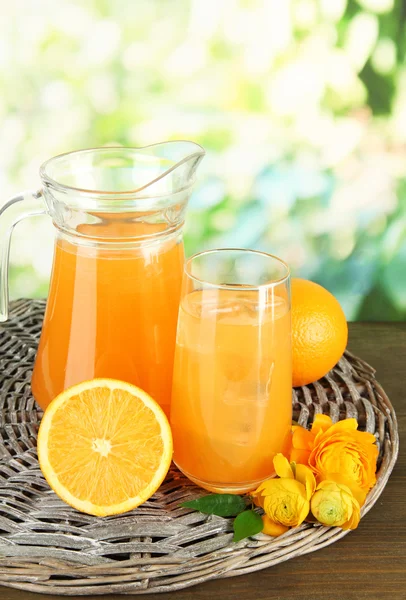 Szkło i dzbanek soku pomarańczowego na drewnianym stole, na zielonym tle — Zdjęcie stockowe