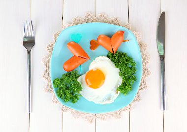 Sausages in form of hearts, scrambled eggs and parsley, on color plate, on wooden background