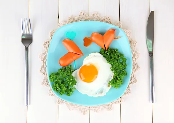 Sausages in form of hearts, scrambled eggs and parsley, on color plate, on wooden background — Stok fotoğraf