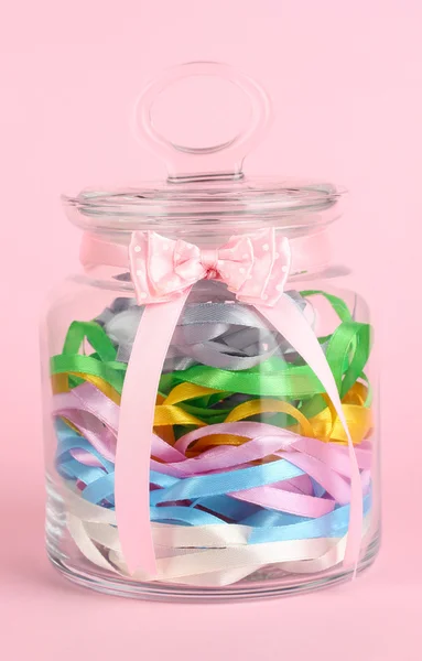 Glass jar containing various colored ribbons on pink background — Stock Photo, Image