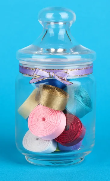 Vaso di vetro contenente vari nastri colorati su sfondo blu — Foto Stock