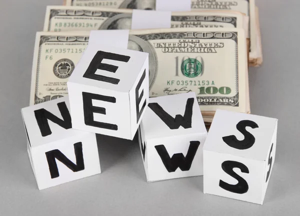 White paper cubes labeled "News" with money on grey background — Stock Photo, Image