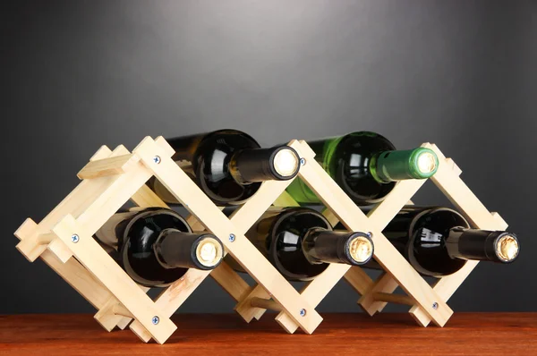 Garrafas de vinho colocadas em suporte de madeira sobre fundo cinza — Fotografia de Stock