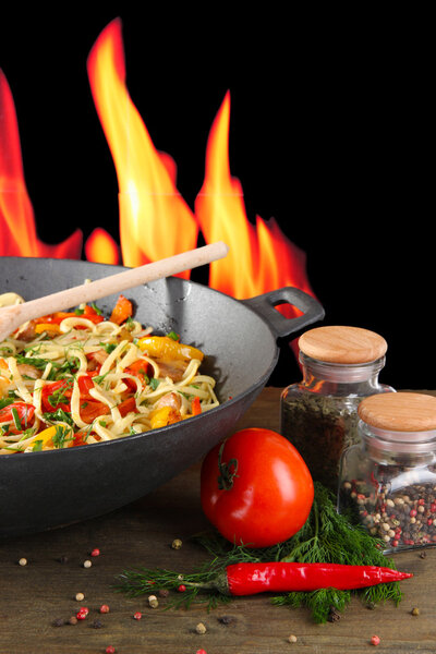 Noodles with vegetables on wok on fire background