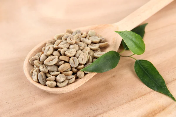 Chicchi di caffè verde in cucchiaio e foglie su sfondo di legno — Foto Stock