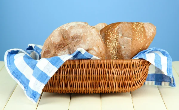 Bread in wicker basket, on wooden table, on color background — Stock Photo, Image