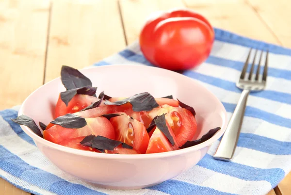 Salad of fresh tomatoes with basil leaves in a bowl on napkin on wooden background — Stock Photo, Image
