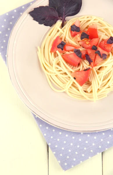 Spaghetti mit Tomaten und Basilikumblättern auf Serviette auf Holzgrund — Stockfoto