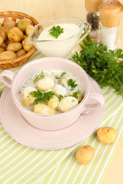 Inschrijving van jonge aardappelen met zure room en kruiden in pan op houten tafel close-up — Stockfoto