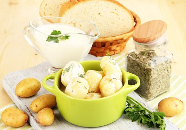 Jeunes pommes de terre tendres à la crème sure et aux herbes dans une casserole sur une planche de bois sur une table close-up — Photo