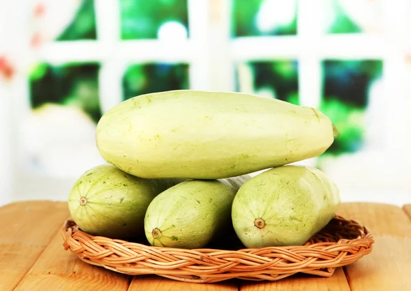 Fresh marrows on wicker mat, on wooden table, on bright background — Stock Photo, Image
