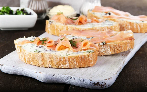 Vis broodjes en kopje thee op snijplank op houten tafel close-up — Stockfoto