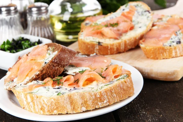 Vissen broodjes op snijplank en plaat op houten tafel — Stockfoto