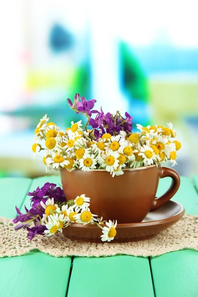 Bouquet of chamomile flowers in cup, on bright background — Stock Photo, Image