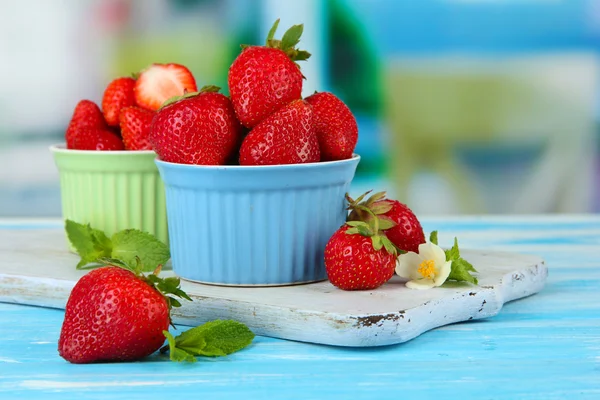 Rijpe zoete aardbeien in kommen op blauwe houten tafel — Stockfoto