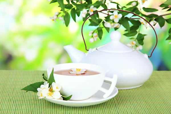 Secangkir teh dengan melati, di atas tikar bambu, dengan latar belakang cerah — Stok Foto