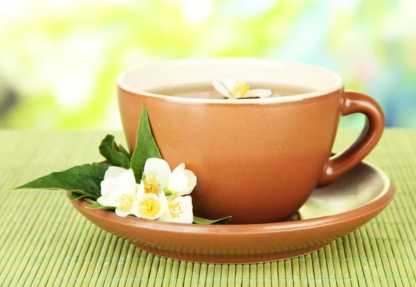 Чашка чая с жасмином, на бамбуковом коврике, на ярком фоне — стоковое фото