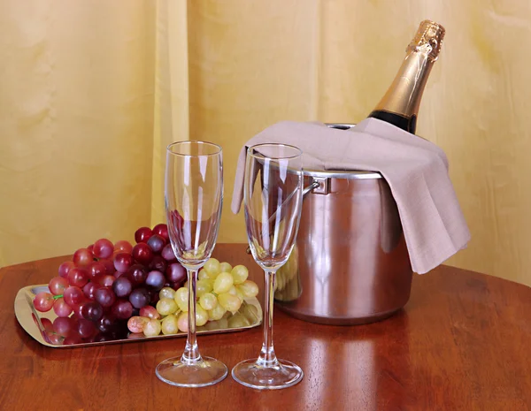 Champagner und Gläser auf rundem Tisch auf Stoffhintergrund — Stockfoto