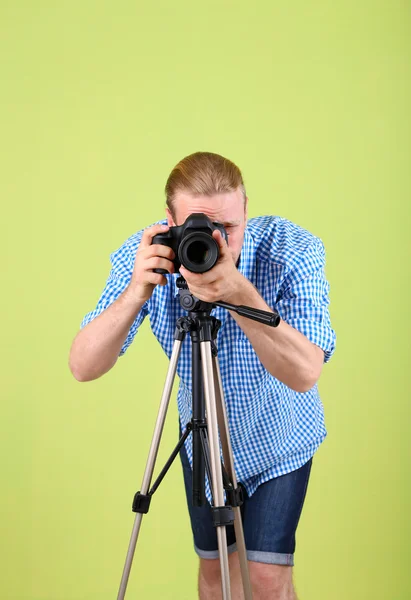 Handsome photographer with camera and tripod, on green background — Stock Photo, Image