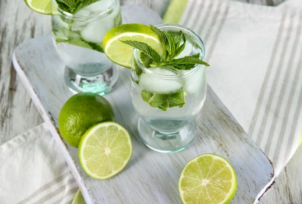 Glasses of cocktail with ice on board on napkin on wooden table — Stock Photo, Image