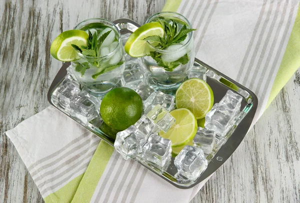 Glazen cocktail met ijs op metalen lade op servet op houten tafel — Stockfoto