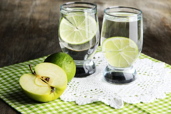 Glasses of cocktail with lime on napkin on dark wooden table — Stock Photo, Image