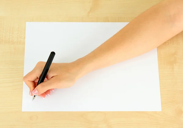 Mão com caneta sobre papel branco, sobre fundo de madeira — Fotografia de Stock