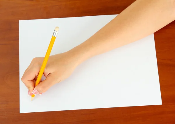 Mano con lápiz sobre papel blanco, sobre fondo de madera — Foto de Stock