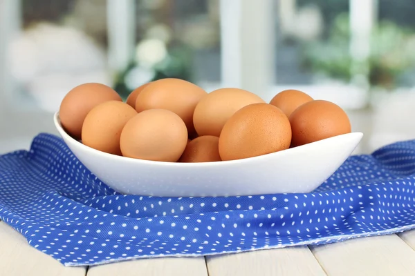Яйца в белой миске на деревянном столе на фоне окна — стоковое фото
