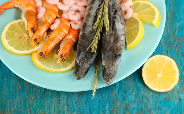 Fresh fishes with shrimp and lemon on plate on wooden table close-up — Stock Photo, Image