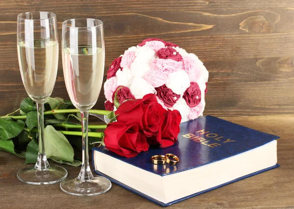 Wedding rings on bible with roses and glasses of champagne on wooden background — Stock Photo, Image