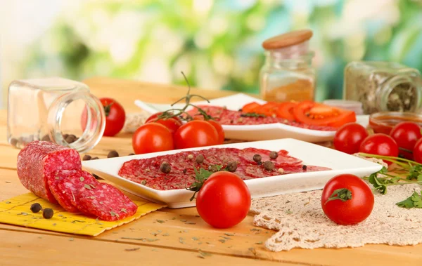 Välsmakande salami på tallrikar på träbord på naturliga bakgrund — Stockfoto