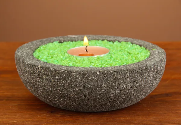 Candle in stone bowl with marine salt, on wooden table, on brown background — Stock Photo, Image