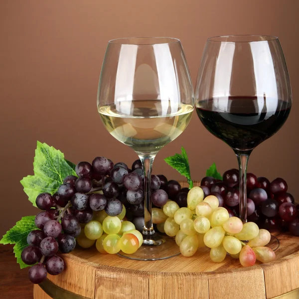 Бокалы красного и белого вина, виноград на деревянном бочке, на цветном фоне — стоковое фото