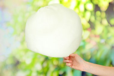 Hand holding stick with cotton candy, on bright background clipart