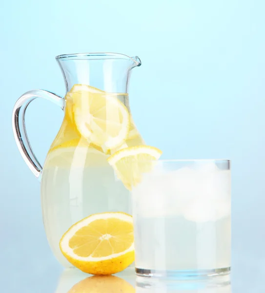 Лимонад в кувшине и стекле на синем фоне — стоковое фото