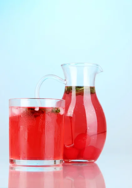 Bebida de cereza en jarra y vaso sobre fondo azul — Foto de Stock