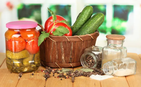 Tasty green cucumbers and red tomatoes in basket, on wooden table on bright background — Stock Photo, Image