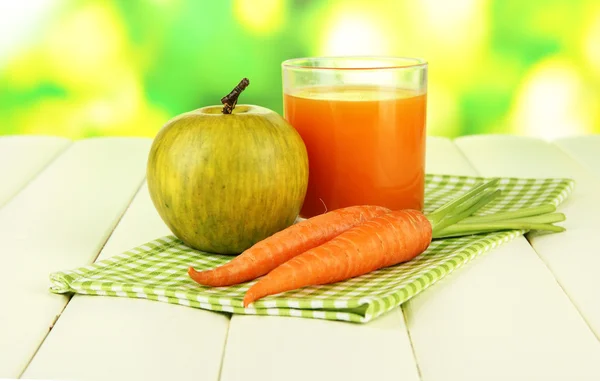 Haufen Karotten und grüner Apfel, Glas Saft, auf farbigem Holztisch auf hellem Hintergrund — Stockfoto