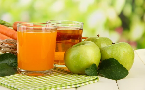 Glas juice, äpplen och morötter på vita träbord, på grön bakgrund — Stockfoto