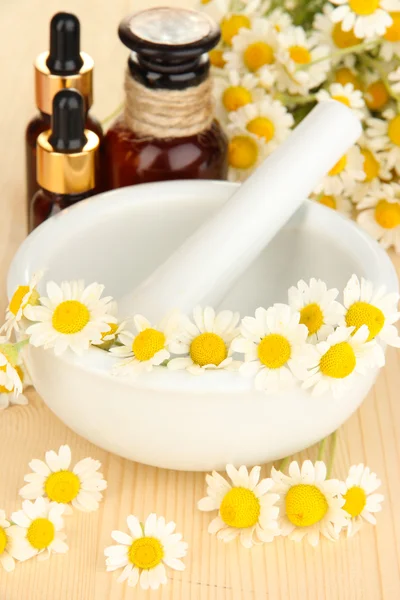 Aceite esencial y flores de manzanilla en mortero sobre mesa de madera —  Fotos de Stock