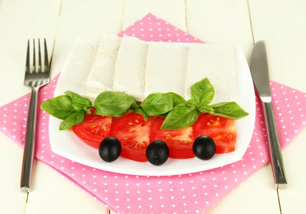 Sheep milk cheese, with basil and tomato on color napkin on wooden background — Stock Photo, Image