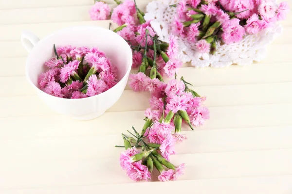 Many small pink cloves in cup and on napkin on wooden background — Stock Photo, Image