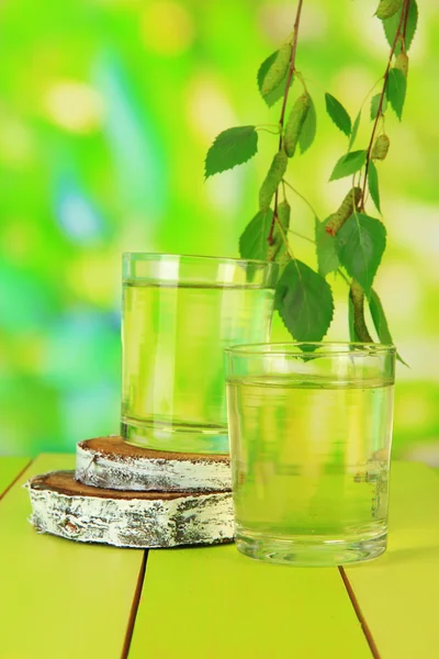 Gläser Birkensaft auf Holztisch, auf grünem Hintergrund — Stockfoto