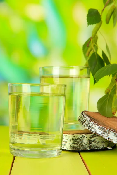 Glasses of birch sap on wooden table, on green background — Stock Photo, Image