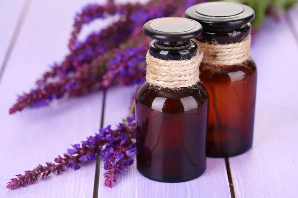 Medizinflaschen und Salvia-Blumen auf lila Holzgrund — Stockfoto