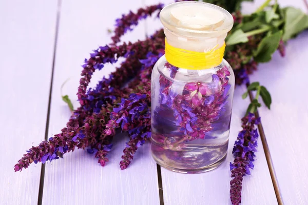 Medizinflasche mit Salvia-Blüten auf violettem Holzhintergrund — Stockfoto