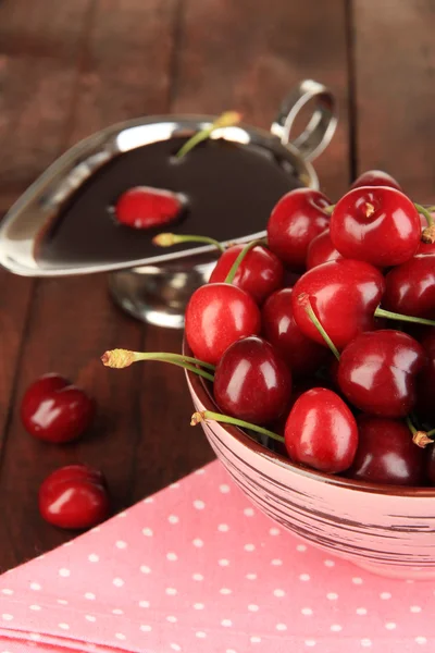 Érett piros cseresznye bogyók, fából készült asztal közelről a tálba, és a csokoládé mártással — Stock Fotó