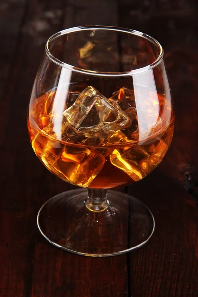 Brandy glass with ice on wooden background — Stock Photo, Image