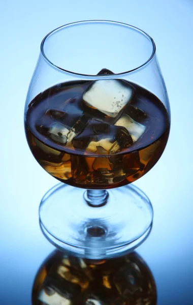 Brandy glass with ice on blue background — Stock Photo, Image